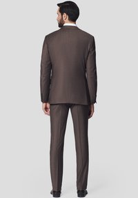 Brąski garnitur o dopasowanym kroju, z pojedynczym rozcięciem i gładką fakturą. Spodnie są prostego kroju z drobnym splotem. Czarne buty dopełniają całość.