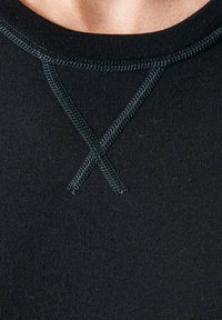 Zwarte aansluitende top met een zachte textuur, geribbelde stof en een X-stikselsontwerp bij de halslijn met contrasterende donkere stiksels.