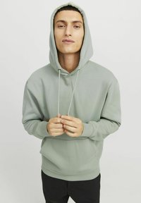 Haut à capuche vert clair avec cordons de serrage, poche avant et poignets côtelés. Texture lisse et coupe standard, assorti avec un pantalon noir.