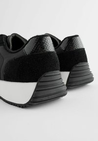 Schwarze Sneaker zeichnen sich durch ein strukturiertes schwarzes Obermaterial mit Wildlederelementen, ein schlankes Design und eine gepolsterte weiße Zwischensohle aus. Strukturierte schwarze Fersenelemente.