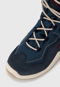 Dunkelblaue Sportschuh mit Wildleder und strukturiertem Stoff, ausgestattet mit cremefarbenen Schnürsenkeln, beiger Sohle und kontrastierenden Steppnähten.