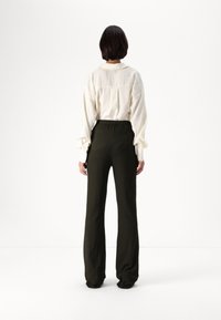 Light beige long-sleeve shirt with a back yoke, paired with high-waisted dark green trousers. Soft texture, relaxed fit, simple design.