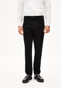 Zwarte denim jeans met een rechte snit, vijf zakken ontwerp en een sluiting met knoop aan de voorkant, gecombineerd met een wit overhemd en zwarte schoenen.