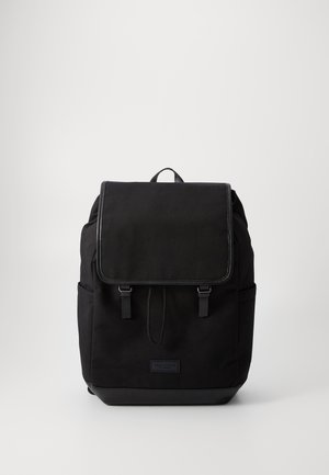 Black fabric backpack featuring a flap closure, two front straps, side pockets, and a textured finish with a leather bottom accent.