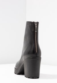 Stivaletto in pelle nera con tacco alto, dotato di una zip laterale, texture liscia e design a punta arrotondata.