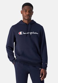 Marine hoodie gemaakt van zachte stof, met een voorzak en een wit logo met rode accenten. Lange mouwen met logo-accenten op de manchetten.