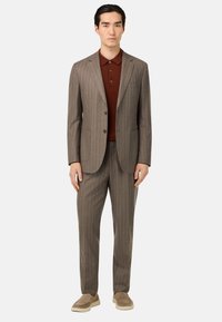 Completo marrone a righe con giacca aderente e pantaloni su misura, abbinato a una polo bordeaux e calzature beige. Tessuto morbido.