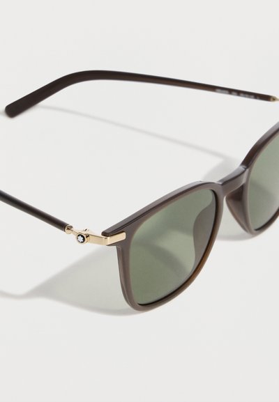 Καφέ ορθογώνια γυαλιά ηλίου με σκουρόχρωμους πράσινους φακούς και χρυσές λεπτομέρειες κοντά στις μεντεσέδες σε λευκό φόντο.