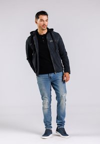 Svart zip-up jacka med huva, bärs över en svart polo, i sällskap med ljusblå slitna jeans och mörka sneakers. Slät textur, avslappnad passform.