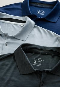 Trei tricouri polo în nuanțile marin, gri deschis și gri închis, cu un material texturat, design cu guler și detalii cu nasturi. Etichetele sunt vizibile în interior.
