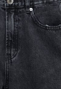 Gros plan sur un jean en denim noir montrant la poche avant, les coutures cousues, la boucle de ceinture et les détails en métal des boutons et rivets.