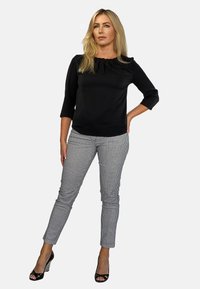 Czarna bluzka z plisowanym dekoltem, trzyczworćowe rękawy; zestawiona z dopasowanymi spodniami w czarno-białą kratę. Założona z czarnymi sandałami na wysokim obcasie.