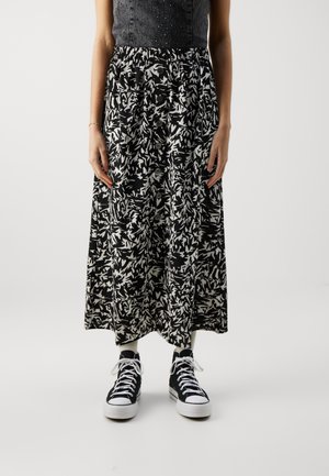 Mujer con una falda midi estampada en blanco y negro con botones en la parte delantera, zapatillas negras altas y calcetines blancos.