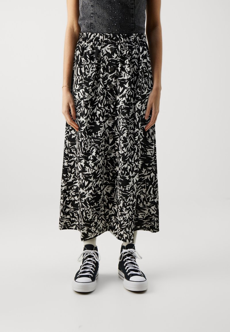 Femme portant une jupe midi à motifs noir et blanc avec des boutons sur le devant, des baskets montantes noires et des chaussettes blanches.