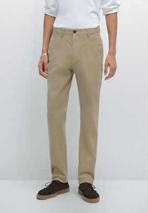 Tan katoen chino's met een rechte pasvorm, voorzien van een enkele knoopsluiting, zijzakken en een gladde textuur. Gecombineerd met donker suède schoenen.