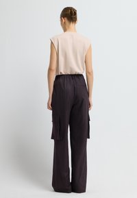 Top corto de color beige claro de manga corta combinado con pantalones cargo de cuadros oscuros que cuentan con dos bolsillos laterales y un corte holgado. Tejido suave y diseño cómodo.