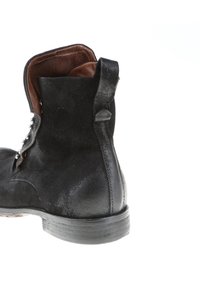 Bottine en daim noir avec bout rond, surface texturée, doublure en cuir marron et petit talon, équipée d'œillets métalliques pour le laçage.