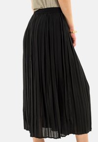 Jupe plissée noire en tissu texturé, avec une taille élastique et un design fluide qui atteint la longueur mi-mollet.