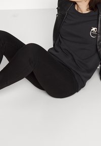 Felpa nera in cotone con logo sul petto, abbinata a jeans skinny neri; presenta una giacca di pelle per aggiungere texture e contrasto.