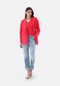 Korallenfarbener Blazer über einem passenden gerippten Oberteil, kombiniert mit hellblauen Jeans mit umgeschlagenem Saum und beigen Sandalen, die einen lässigen, entspannten Schnitt aufweisen.