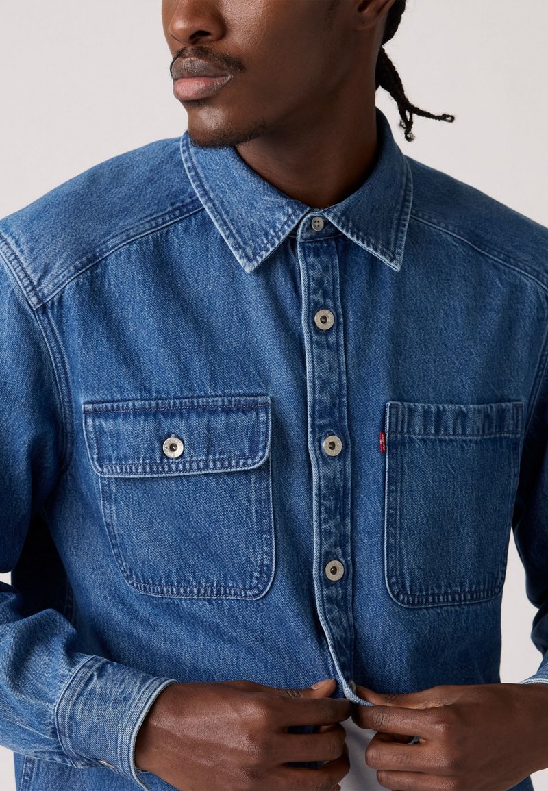 Blauwe denim overhemden met een gekraagde halslijn, twee borstzakken en zilveren knoopsluitingen. Geweven stof met een klassieke pasvorm.