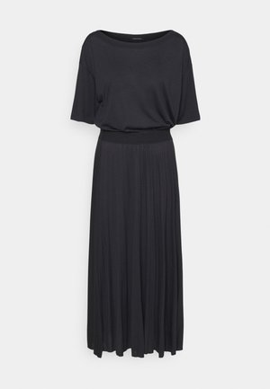 Robe noire à manches courtes, taille ajustée et longue jupe plissée sur fond clair uni.