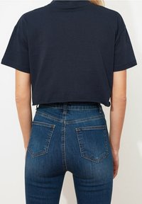 Marinblå kortärmad t-shirt som är avkortad, ihop med högmidjade blå jeans med bakfickor och en figursydd design.