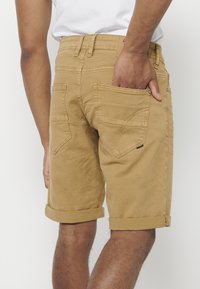 Shorts khaki en coton, avec un ourlet retroussé, des poches arrière et une coupe ajustée. Couture visible et détail de marque subtil.