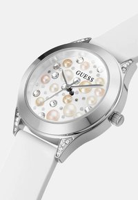 Zilveren Guess-horloge met witte band, versierd met parel- en kristalaccenten op de wijzerplaat en de rand van de kast.