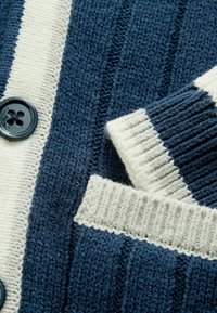 Námořnický pruhovaný pletený cardigan v krémových a tmavě modrých odstínech, s žebrovaným límcem, zapínáním na knoflíky a texturovanou tkaninou s boční kapsou.