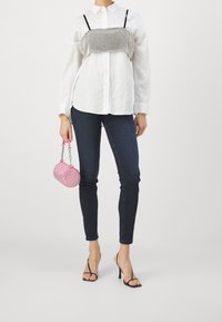 Camisa blanca de botones, combinada con un top corto negro y plateado brillante, junto con unos jeans oscuros y un bolso circular rosa. Tacones negros.
