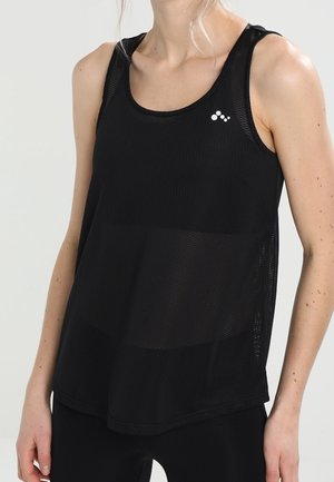 Kvinde iført en sort, ærmeløs atletisk tanktop i mesh med en lille hvid logo på venstre bryst mod en ensfarvet lys baggrund.