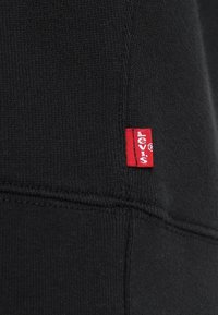 Tissu en maille noire avec une petite étiquette de marque Levi's rouge cousue dans la couture près du bord inférieur du vêtement.