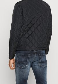 Schwarze, gesteppten Jacke mit Taschen im Seitenzipper, ausgestattet mit einem Stehkragen und gerippten Bündchen, kombiniert mit dunkelblauen Jeans.