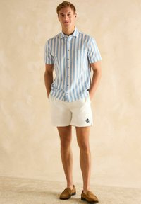 Lühikeste varrukatega helesinine ja valge triibuline särk, millel on nööbid ja rinnatasku, koos valgete lühikesete pükste ja pruunide mokasitöölistega.