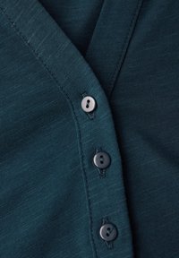 Tissu en coton teal avec une texture côtelée, présentant un design en V et quatre boutons gris foncé sur le devant.