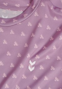 Zbliżenie na jasnofioletową tkaninę z małymi kwiatowymi wzorami i dwoma białymi szewronami blisko środka, pokazującymi okrągłą krawędź dekoltu.