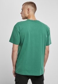Tricou din bumbac verde, cu mâneci scurte și guler rotund, având un croi lejer și cusături uniforme. Fără modele sau accente proeminente.