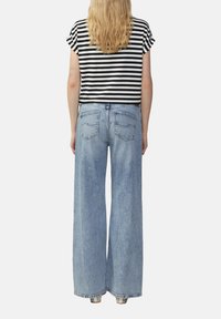 Schwarz-weiß gestreiftes Kurzarmoberteil kombiniert mit hoch geschnittenen, weiten hellblauen Jeans. Sichtbare Gesäßtaschen mit minimalem Nähdetails.