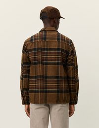 Chemise en flanelle à carreaux marron avec des accents noirs et rouges, présentant des poignets à bouton et un ourlet droit. La vue arrière montre une coupe décontractée et une texture douce.