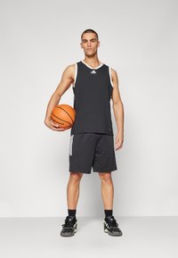 Černá sportovní tank top a šortky s bílými akcenty, na bocích se třemi pruhy, držené oranžovým basketbalem. Černé tenisky.