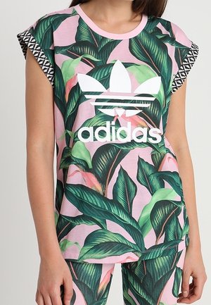 Różowa koszula z krótkimi rękawami z wzorem tropikalnych liści i białym logo Adidas. Czarne wzorzyste akcenty wzdłuż rękawów.