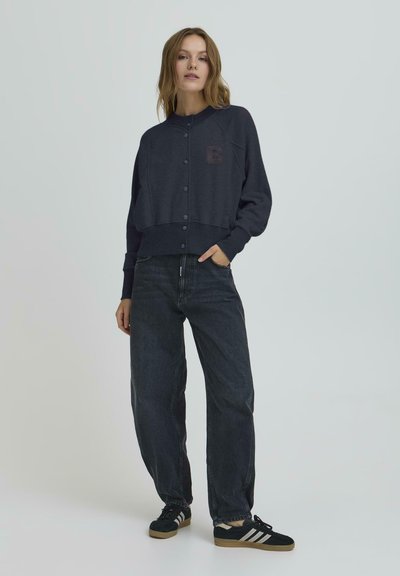 Tamsiai mėlynas sutrumpintas džemperis su mygtukų uždarymu ir subtiliu 'B' logotipu, derinamas su aukštu liemeniu juodomis džinsų kelnėmis ir juodais sportbačiais.