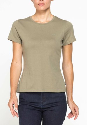 Donna che indossa una maglietta verde oliva aderente a maniche corte e jeans blu scuro, mostrata dalle spalle ai fianchi su sfondo bianco.