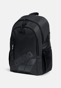 Zaino nero in tessuto strutturato, dotato di due scomparti con cerniera, una tasca laterale e un grande logo. Spallacci imbottiti regolabili.