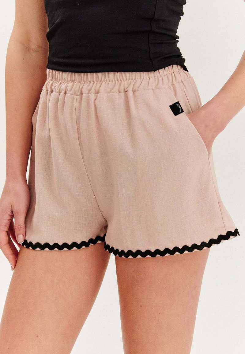 Svetloružové šortky vyrobené z textúrovanej látky, s elastickým pásom a čiernym volánkovým lemovaním na leme. Obsahujú bočné vrecká.