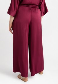 Burgunderfärgade vida byxor i texturerad tyg med elastisk midja, som har en avslappnad passform och en slät finish.