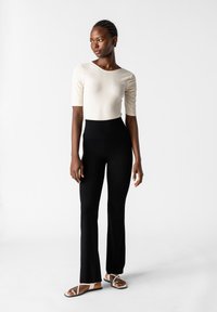 Crème kleurige ribgebreide top met korte mouwen, gecombineerd met hoge taille zwarte flared pants, afgemaakt met platte sandalen met banddetail.