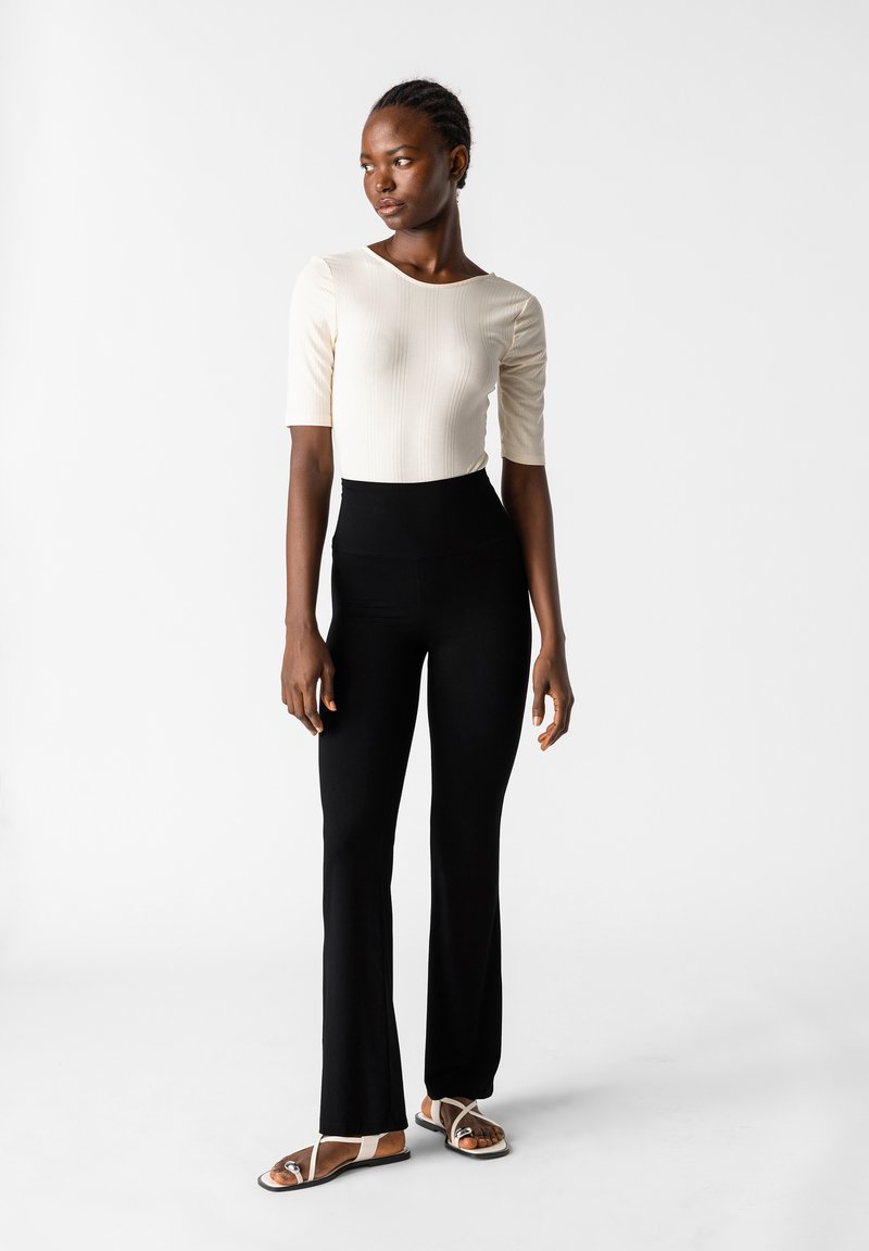 Crème kleurige ribgebreide top met korte mouwen, gecombineerd met hoge taille zwarte flared pants, afgemaakt met platte sandalen met banddetail.