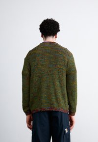 Green knit sweater with multicolored specks, ribbed texture, and a round neckline. Features long sleeves and a loose fit.